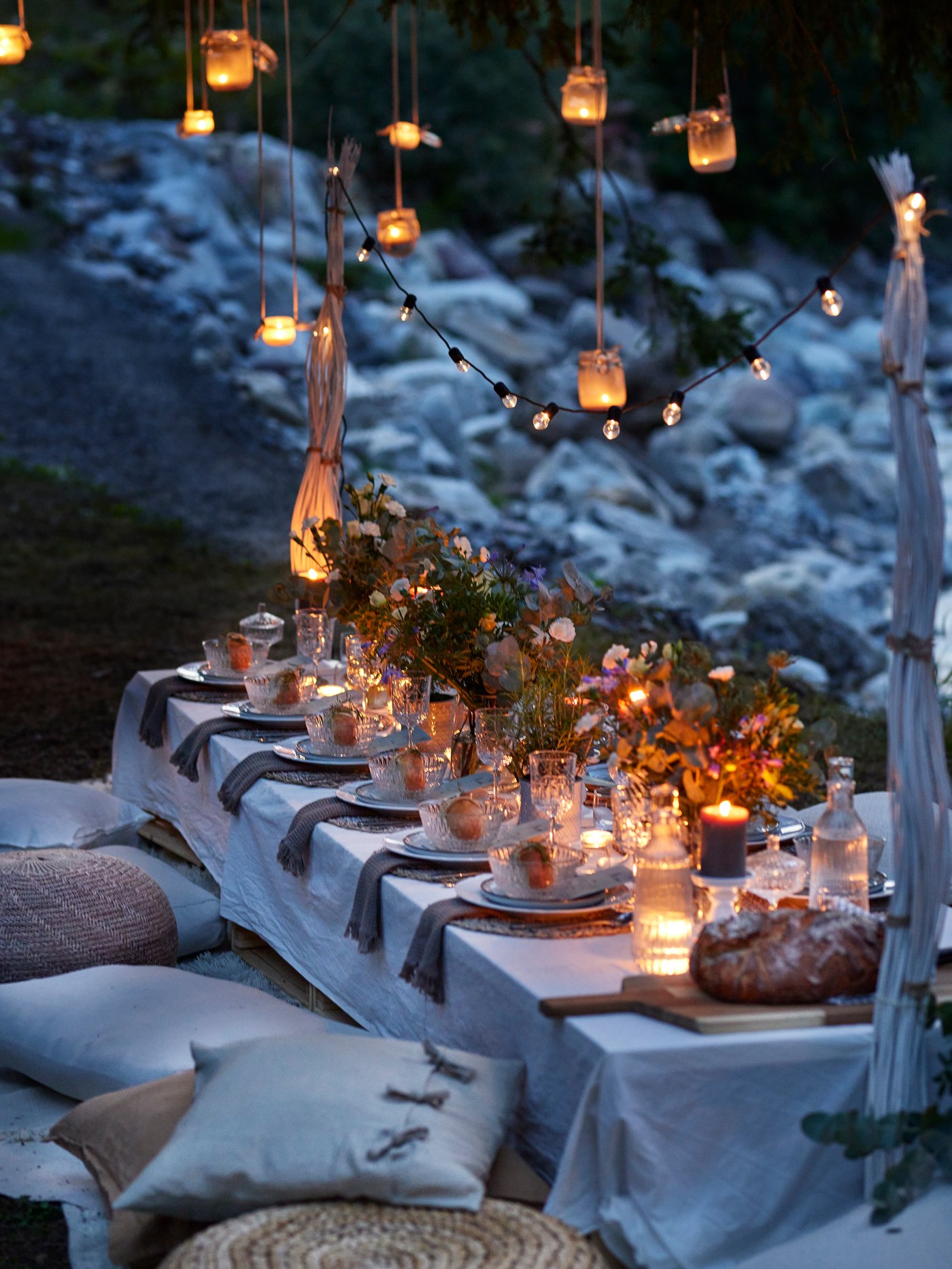 En kvällsbild på ett festligt dukat långbord utomhus med massor av ljus, lyktor och slingor.