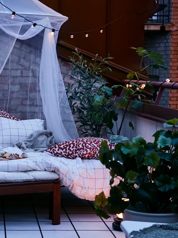 Una terrassa a l'aire lliure al capvespre amb un niu acollidor format per una gandula, una mosquitera, una catifa, fanalets i una garlanda de llums d'exterior.