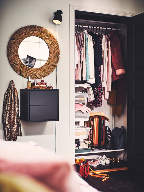 Bedroom with open closet, mirror, and small cubic dark grey wooden cabinet with 2 drawers mounted on the wall.