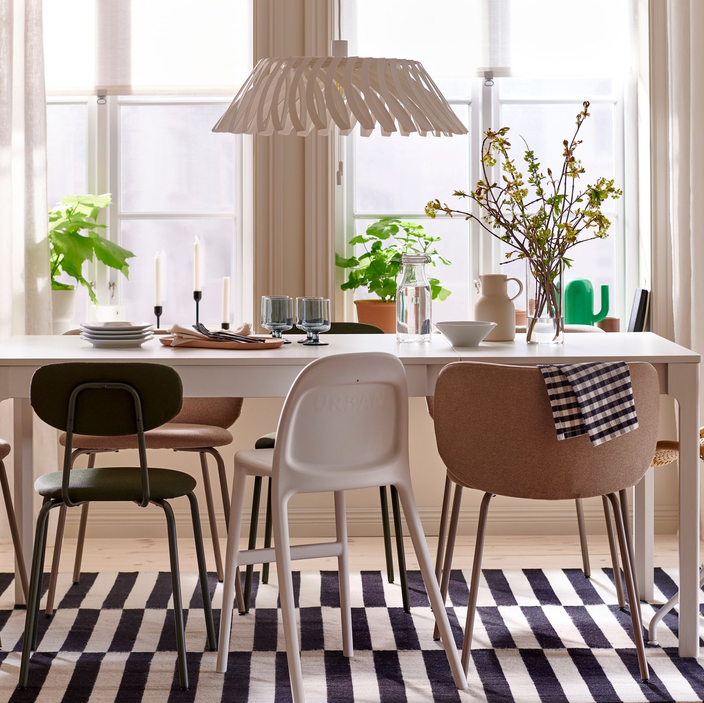 A white EKEDALEN extendable table is placed on a black and white rug and there are chairs in different styles around it.