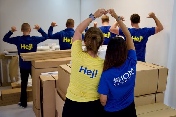 Wolontariusze z IKEA i Międzynarodowej Organizacji ds Migracji na tle paczek z meblami