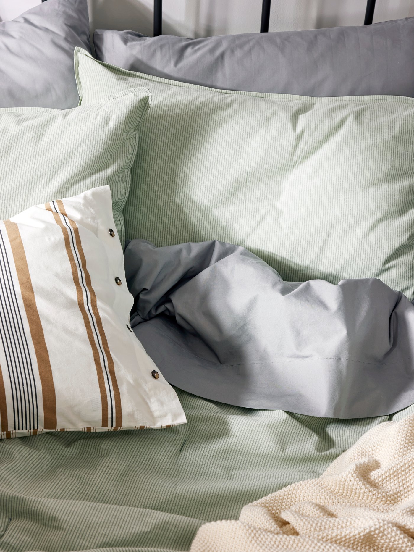 Close-up of bed with unmade bedding in light green, grey and beige.