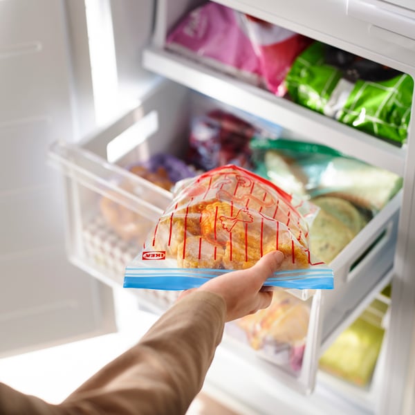 A close-up featuring a hand demonstrating using ISTAD resealable bags to store foods inside the freezer.