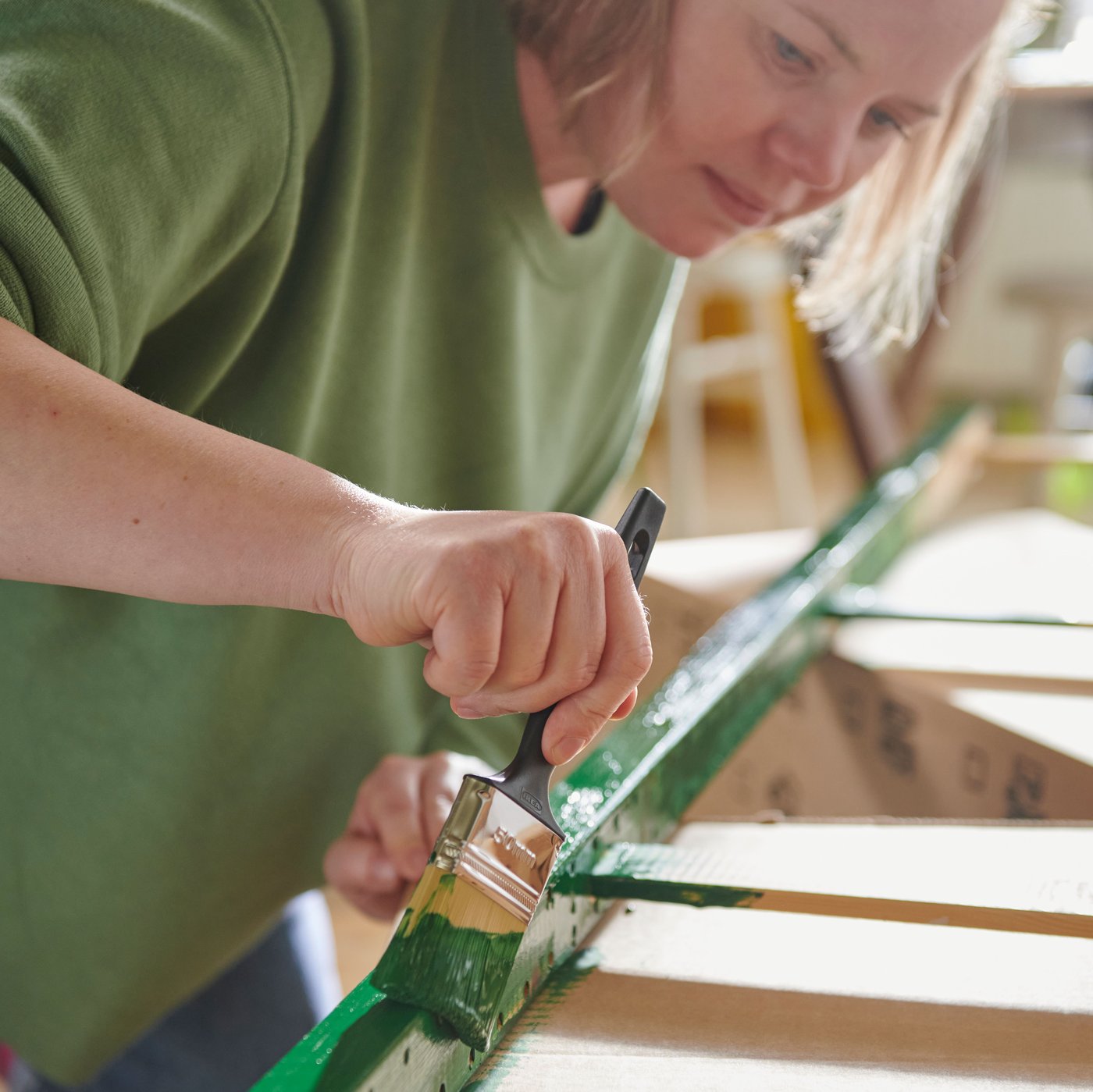 A person applies green paint to the edge of an IVAR shelving unit, showing that the solid wood can be painted.