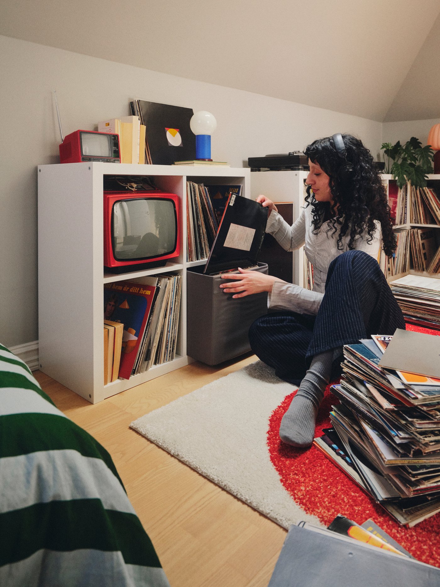 A person wearing headphones puts a record into a storage box that is in a white KALLAX shelving unit with four compartments.