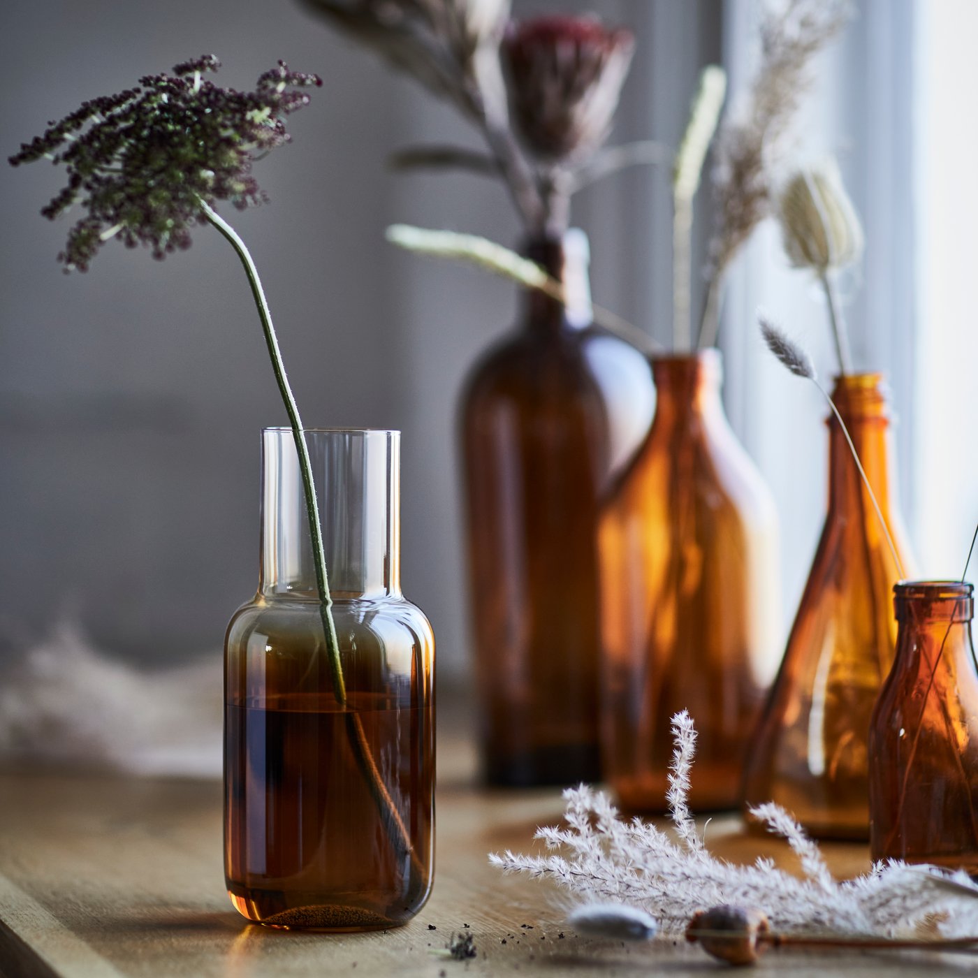 A brown HÖSTAGILLE vase holding a dried flower, elegantly placed on a wooden table with soft ambient light.