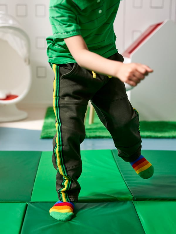 Child playing on bright green PLUFSIG folding gym mat on the floor, IKEA PPS LÖMSK swivel armchair in back.