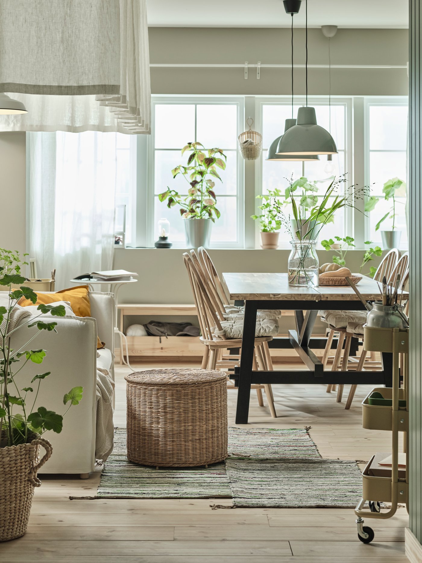 A kitchen with a SKOGSTA dining table, and chairs, 2 lit pendant lamps above, and a pouffe with storage beside a 2-seat sofa.