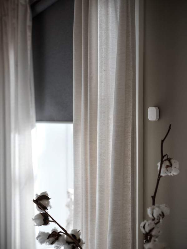 TRÅDFRI remote attached to a grey wall is connected to FYRTUR block-out blind.