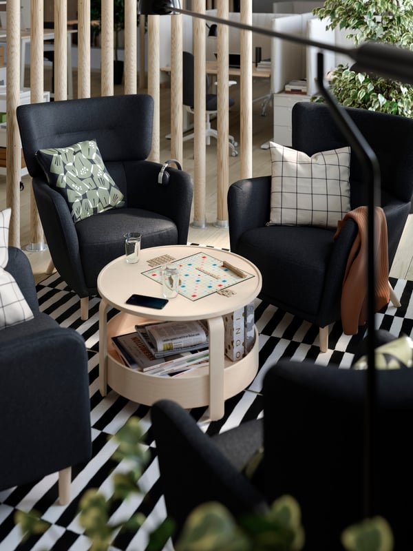 Four OSKARSHAMN wing chairs in Gunnared black-grey, with decorative pillows, are placed around a round coffee table.