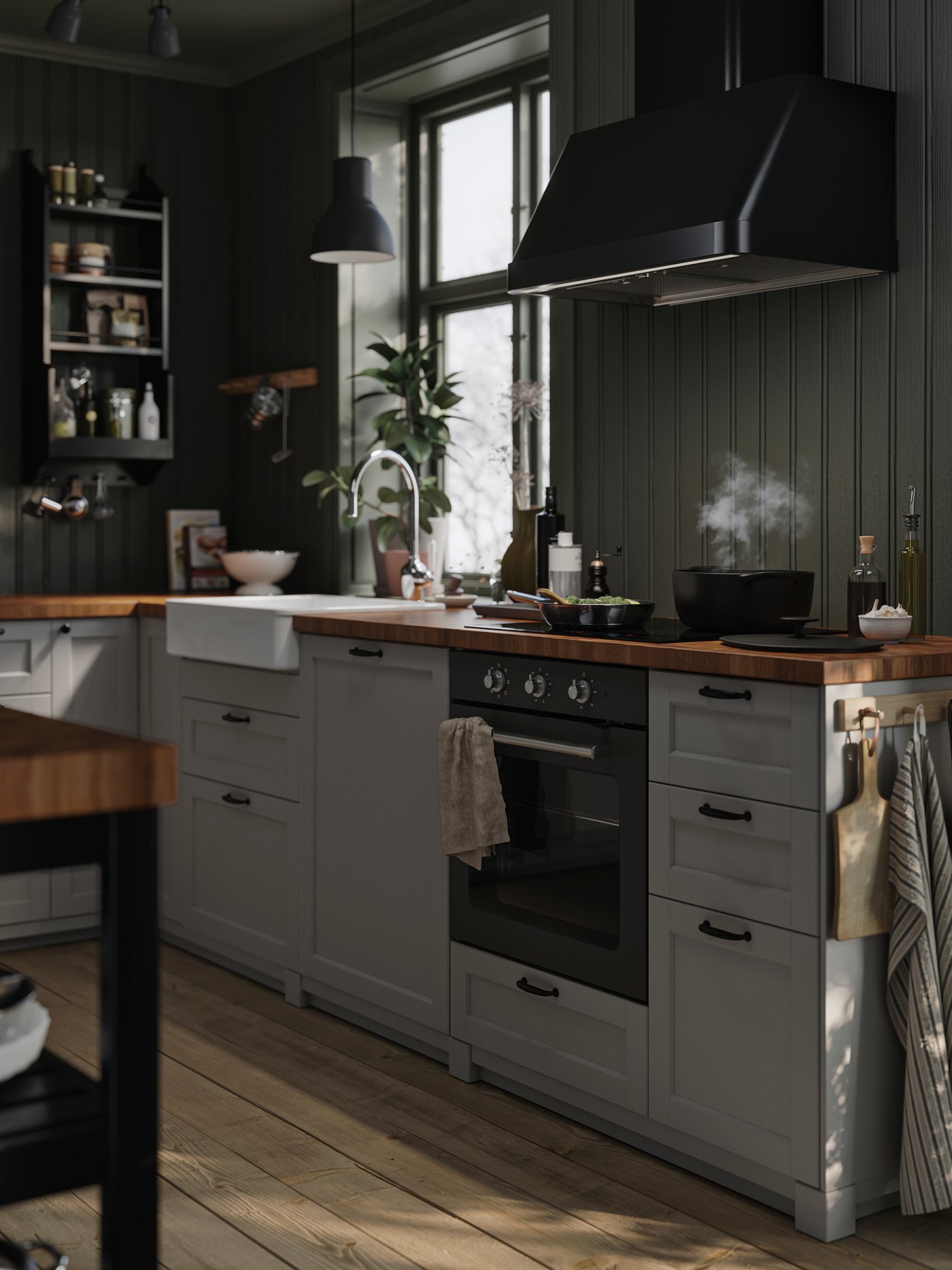 Modernt kök med vita skåp, mörkgröna väggar, ånga från gryta på spisen och naturligt ljus från fönstret.
