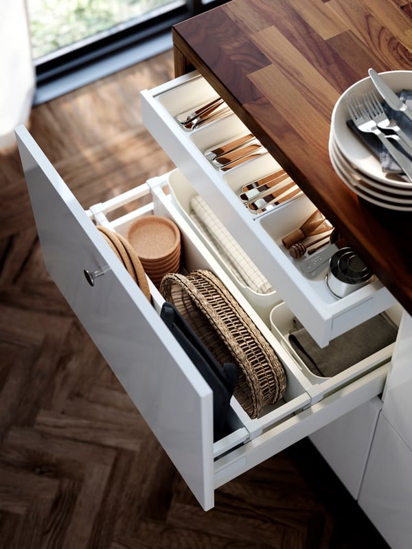 A large drawer in a cabinet with white RINGHULT kitchen fronts is pulled out and there are kitchen items organised inside.