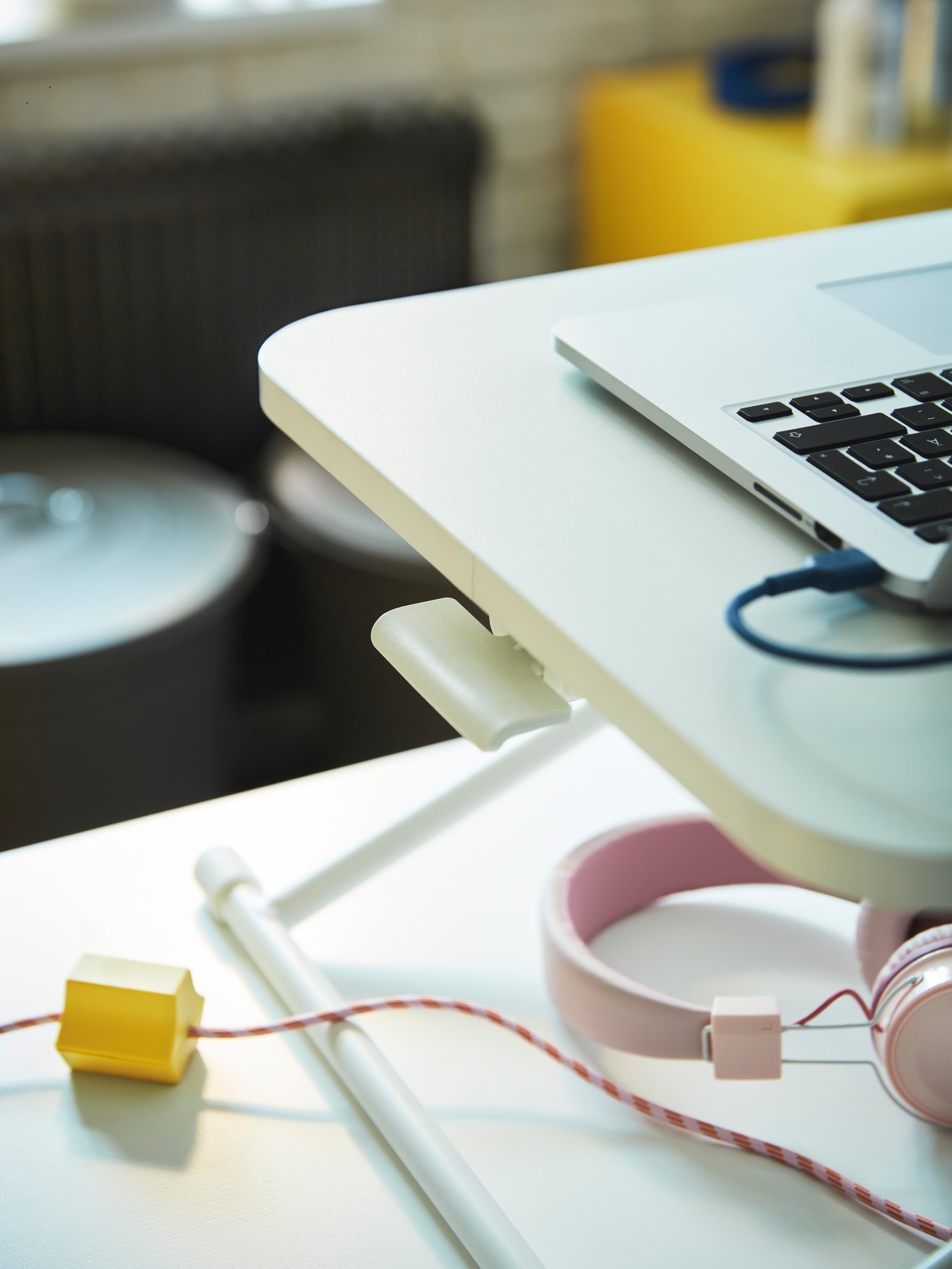 A weighted yellow HÅVSKAL USB anchor holds a striped cord in place underneath a laptop on a DUBBLA laptop stand.