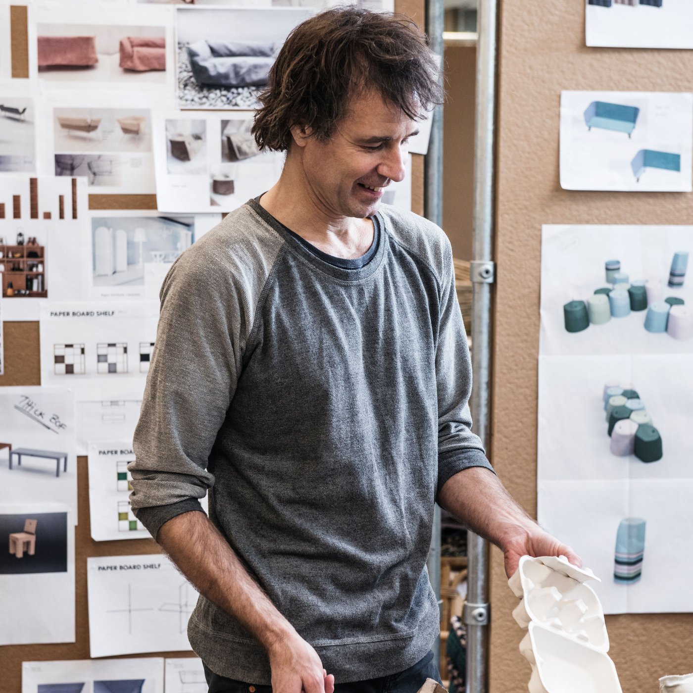 A designer is examining wood pulp products in front of large wall boards with designer drawings.