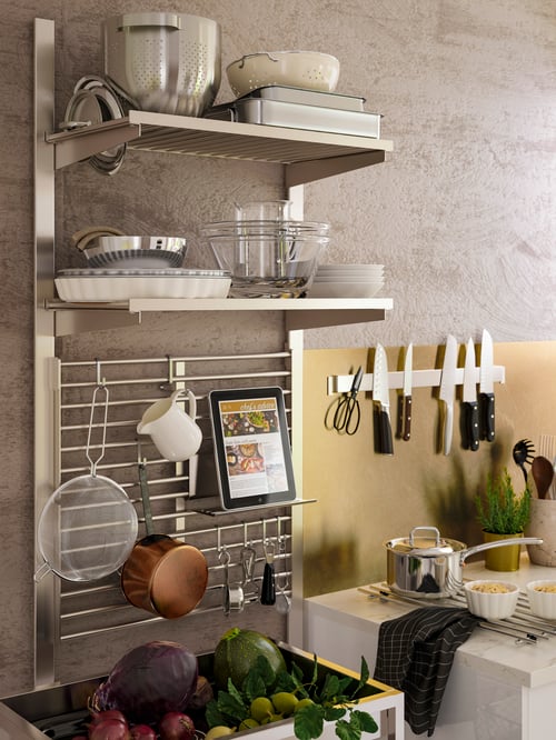 A stainless steel KUNGSFORS suspension rail with shelves and a wall grid is used to store cookware and hanging utensils.