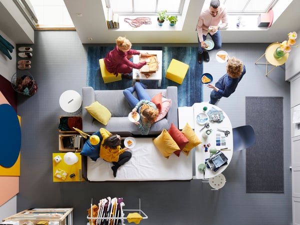 Top view over a group of people eating pizza in a livingroom with grey floor.