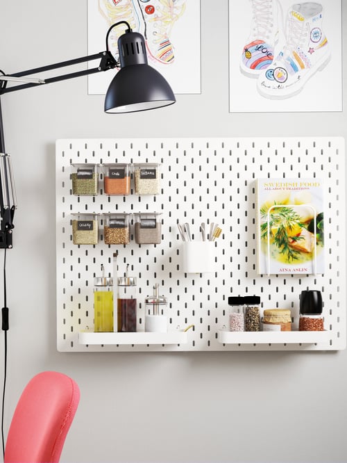 Fotografie largă a unui pegboard cu containere, rafturi, containere cu capac și o imagine, cu o veioză de lucru în lateral.