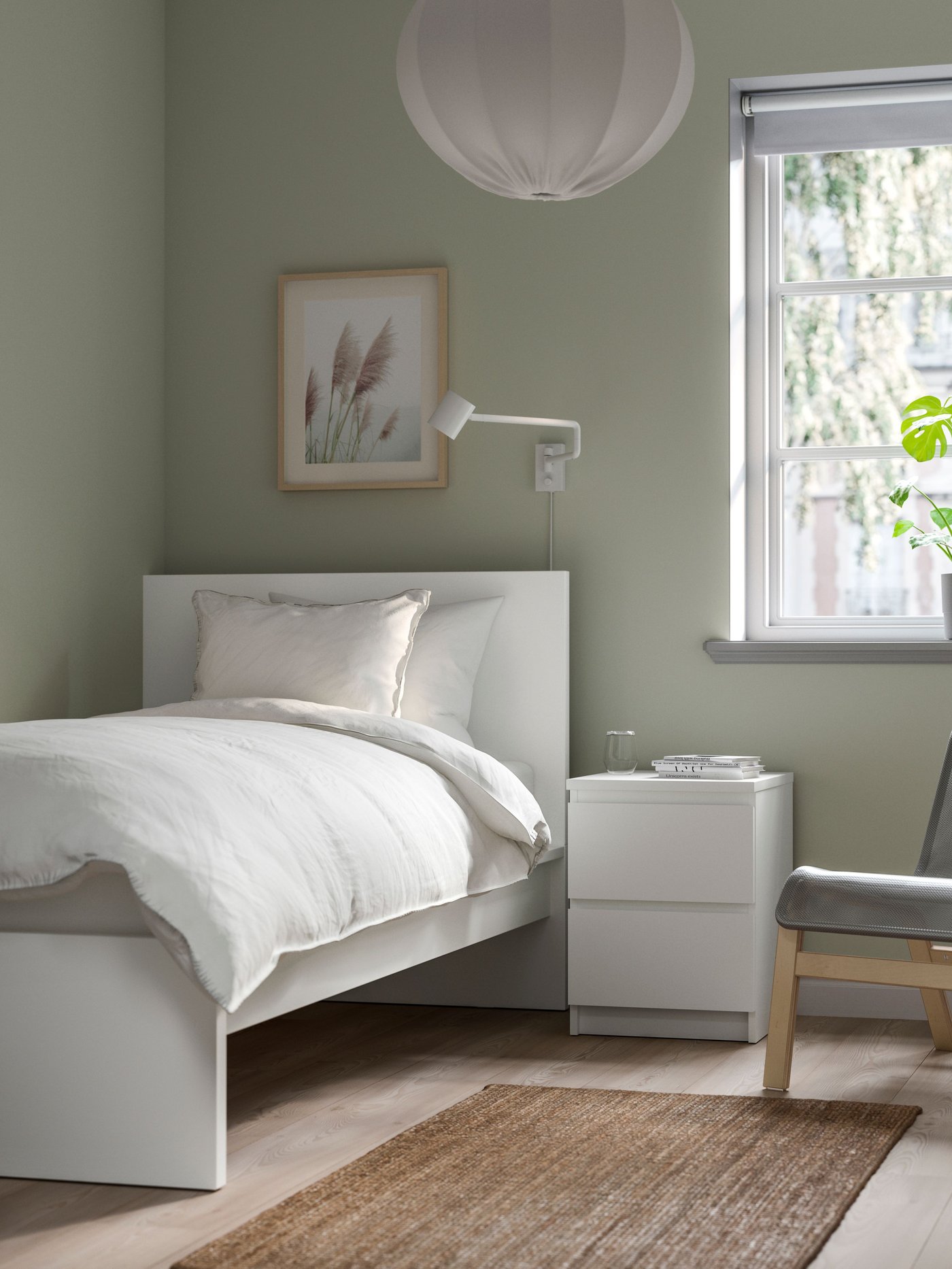 Un dormitorio con una cama MALM blanca con ropa de cama y almohadas blancas. Al costaado de la cama una mesita de noche con dos cajones. 