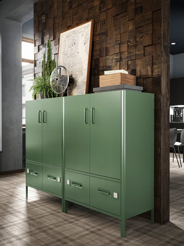 Two large IDÅSEN cabinets in green with doors and drawers, standing next to each other in a warmly lit office.