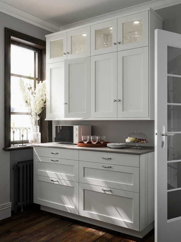 Armoires de cuisine avec portes ENKÖPING et panneaux de finition en effet bois blanc près d’une fenêtre, un four à micro-ondes et des articles sur le comptoir.