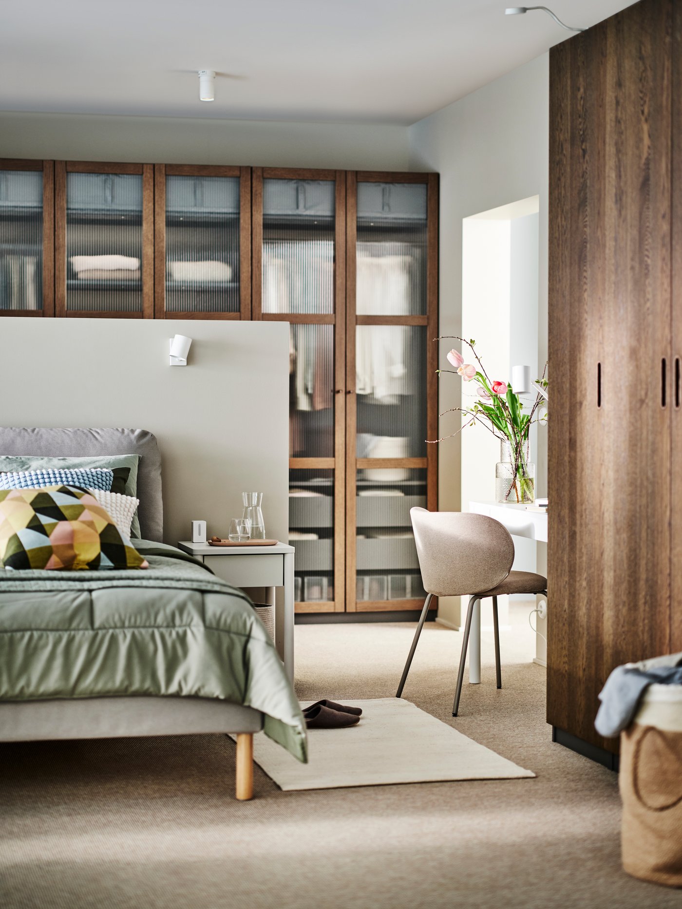 Ein braunes Polsterbett SAGESUND, bezogen mit einer grünen HEDFRYLE-Bettdecke und einem Kissen mit einem mehrfarbigen SVARTHÖ-Bezug.