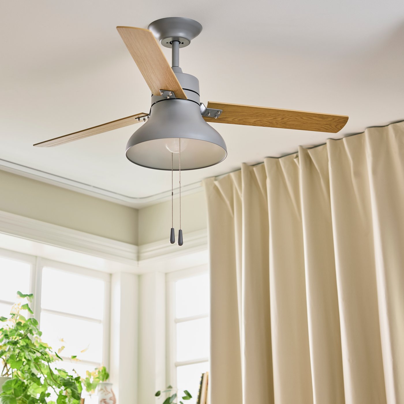 An AKTERSTAGAD ceiling fan with light wood effect, mounted to the ceiling in a room with block-out curtains.