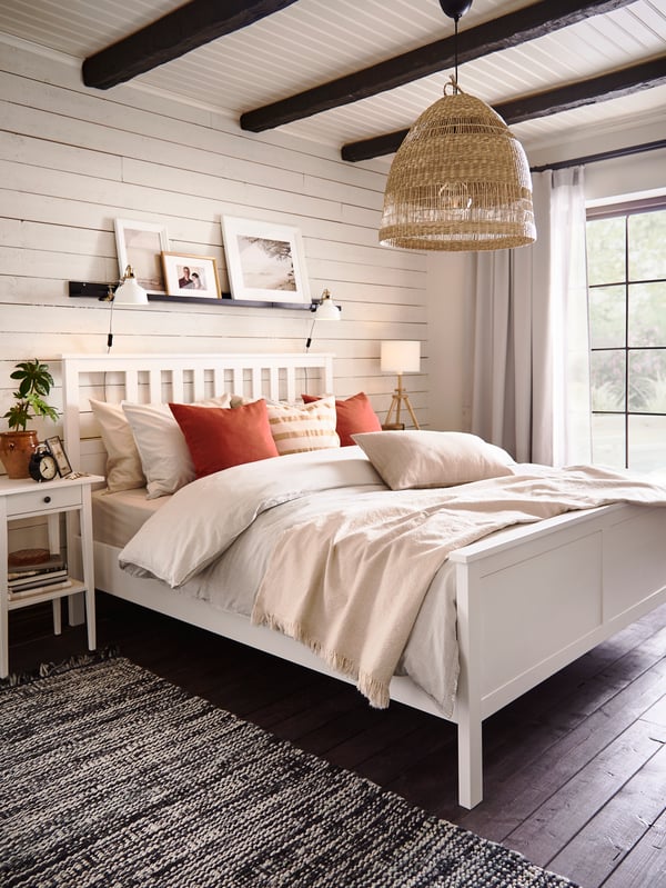 Une chambre à coucher avec un lit HEMNES blanc assorti d’une table de chevet HEMNES. Un tapis tissé se trouve près du lit.