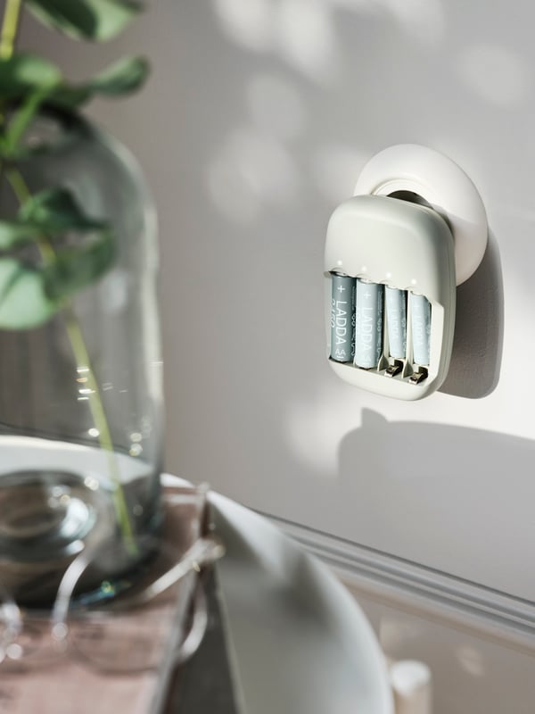 En batteriladdare LADDA som laddar batterierna medan den är ansluten till ett runt vägguttag i en ljusgrå vägg.