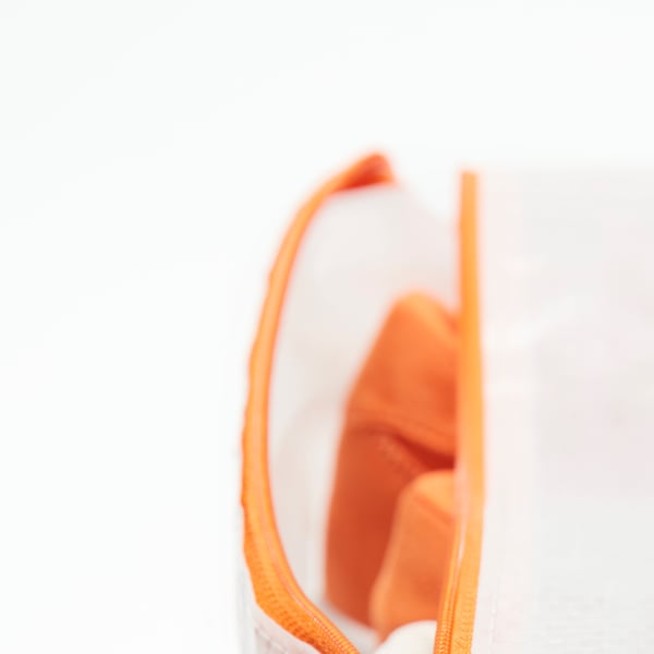 A close-up of an opened zip on a PÄRKLA shoe bag revealing a pair of orange casual shoes. A section of a larger image.