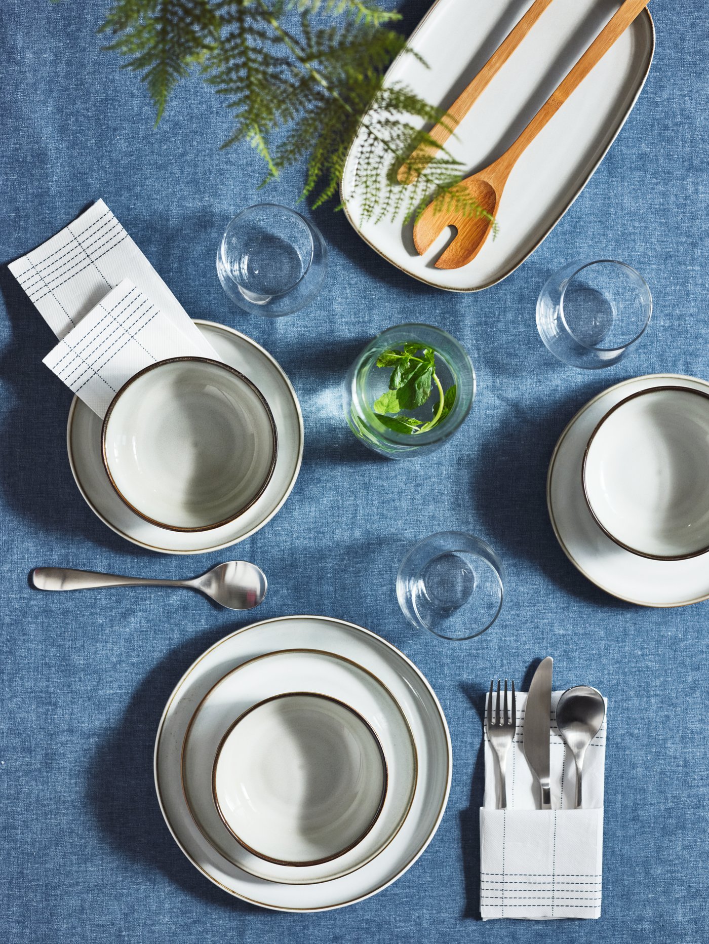 Vasos STORSINT sobre mantel azul y junto a los platos blancos GLADELIG.