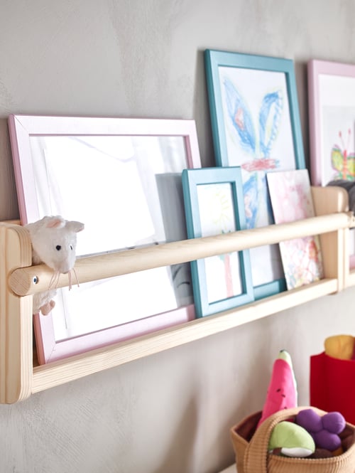 FLISAT wall storage holding framed children’s pictures and a soft toy mouse.