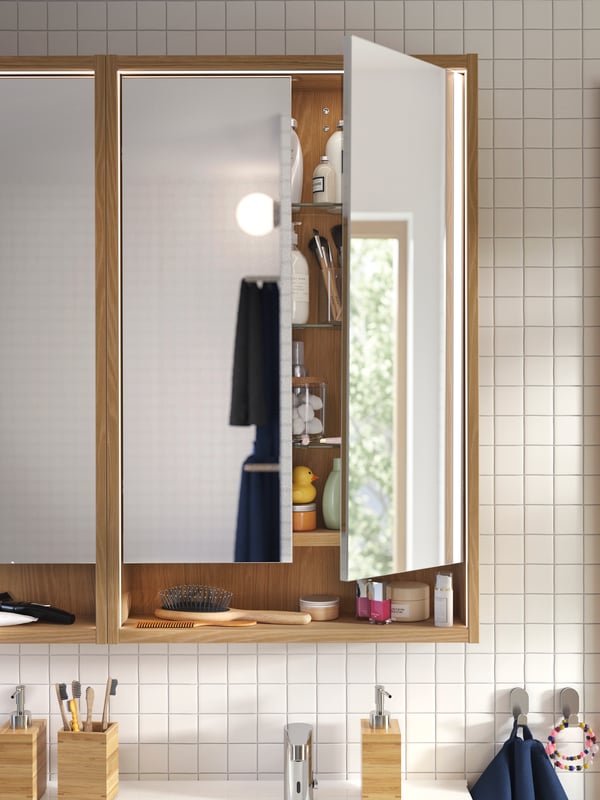 Two FAXÄLVEN mirror cabinets with built-in lighting, in oak, mounted on a white tiled bathroom wall above a sink.