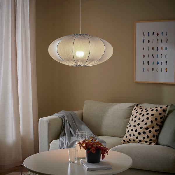 A turquoise REGNSKUR pendant lamp hangs over a table which stands in front of a sofa against a wall in a living room.