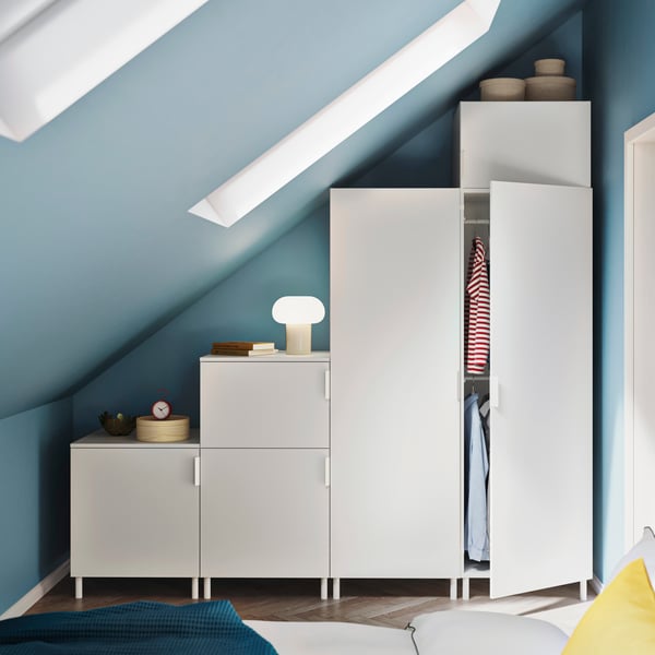 In a room painted in light blue, a white PLATSA wardrobe with six doors stands under a sloping ceiling with skylights.