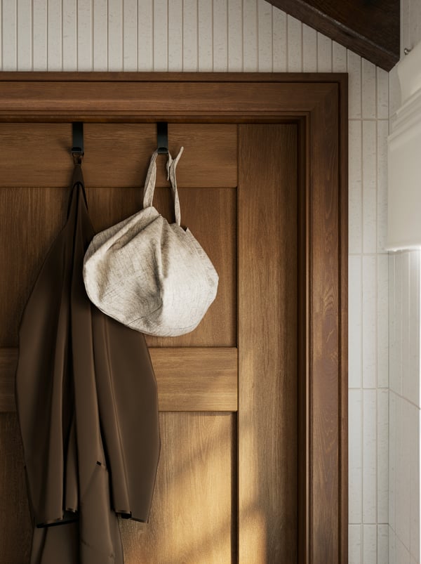 A brown door has two black SKOGSVIKEN hooks with a brown bathrobe hanging from one of them and a white bag from the other.