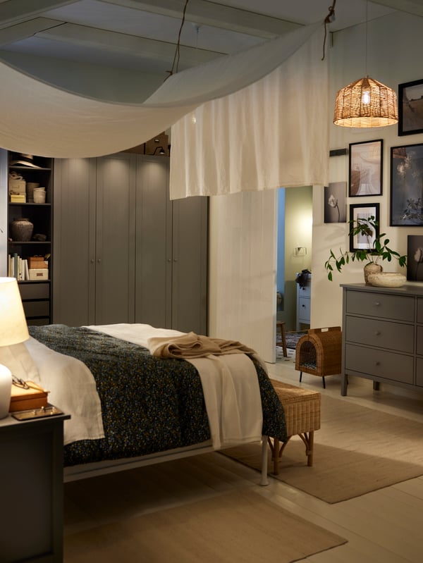 A bed covered in a ROSENTIBAST 3 comforter and a white bedspread in front of a PAX/GULLABERG wardrobe in a dimly let bedroom.