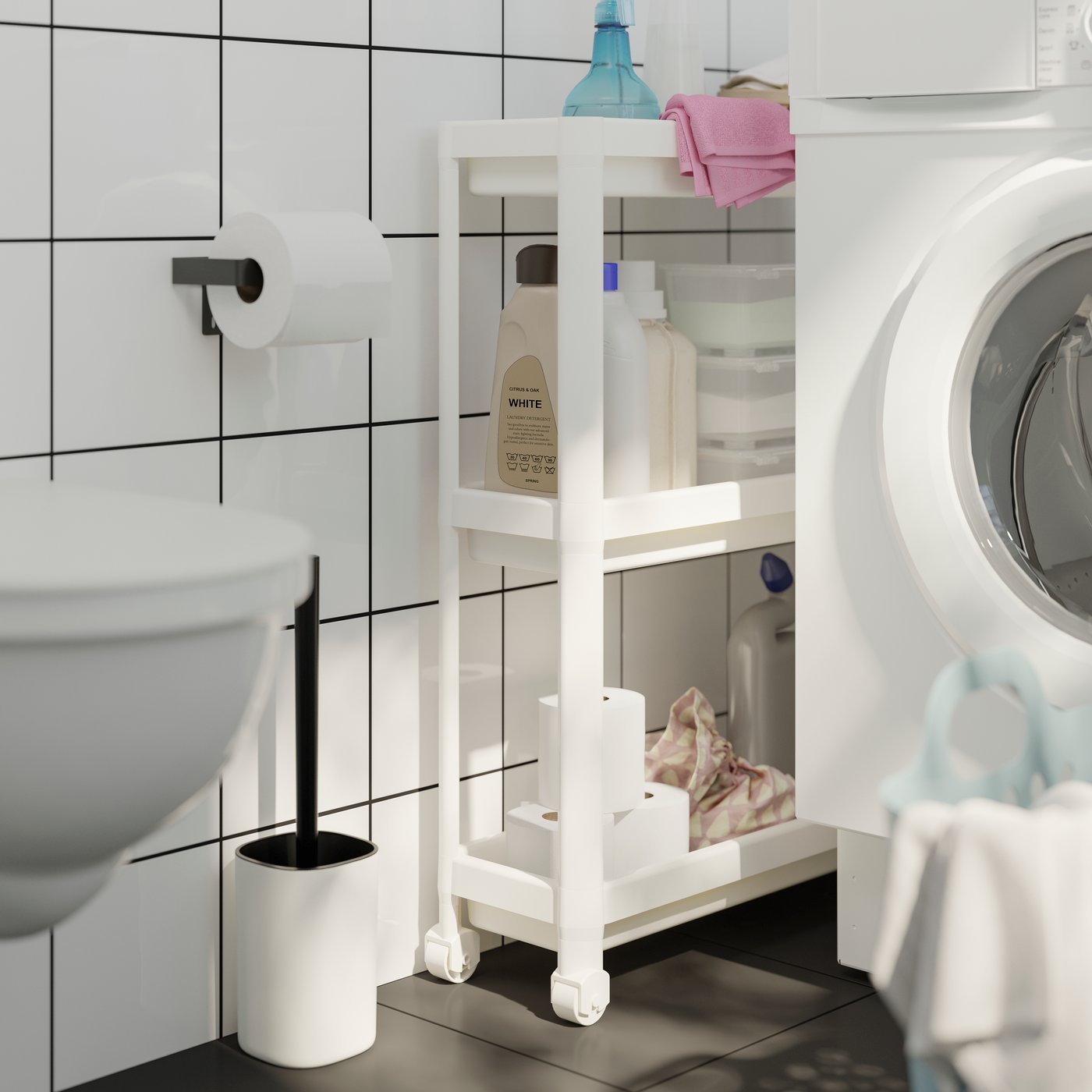 A narrow VESKEN trolley with three shelves filled with cleaning essentials and toilet paper rolls, next to a washing machine.