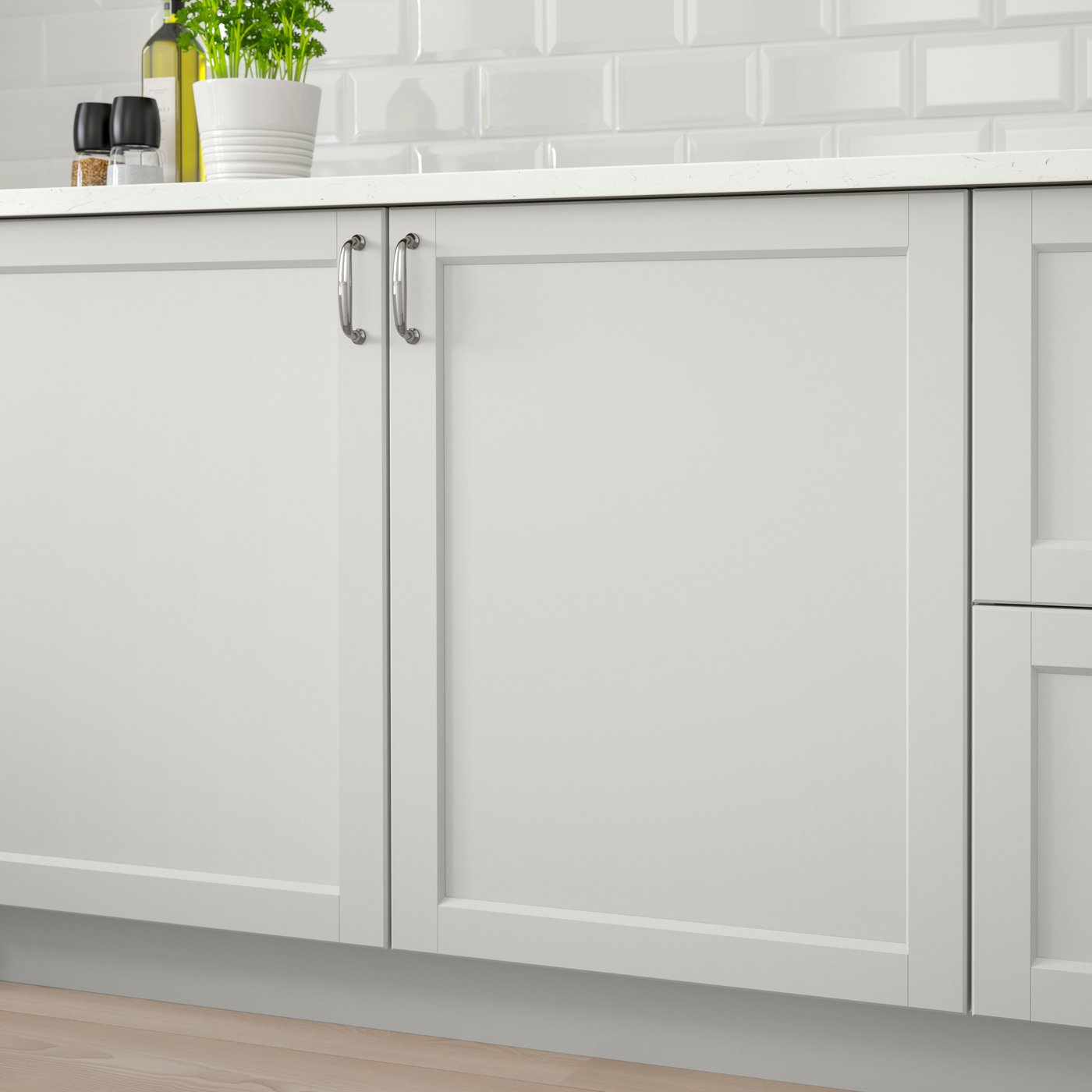 Køkenskabe med lysegrå LERHYTTAN køkkenfronter med facetskårne kanter og indbyggede paneler og greb i rustfrit stål samt en hvid bordplade hvor der står en grøn plante i en hvid urtepotteskjuler.