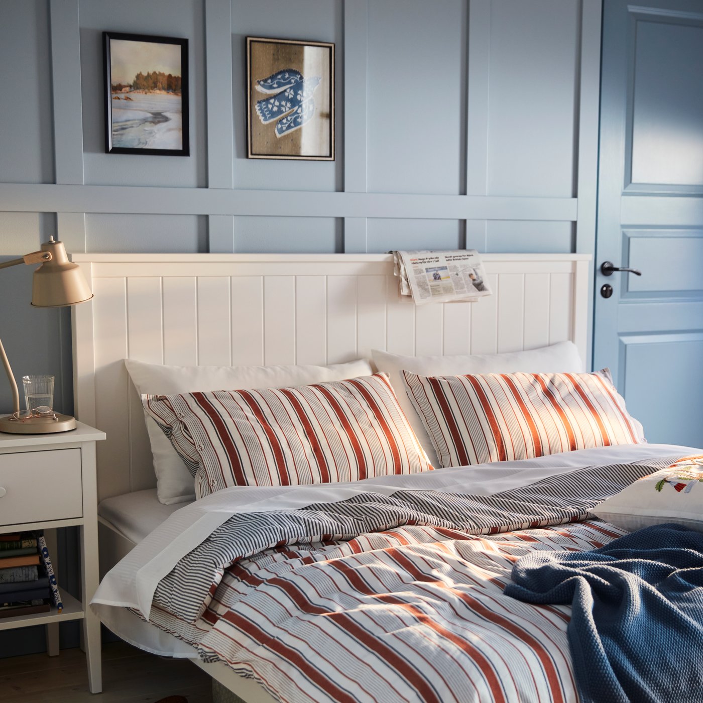 A blue painted bedroom with a GULDAKLEJA bedlinen set in red-brown and white stripes on a white bed.