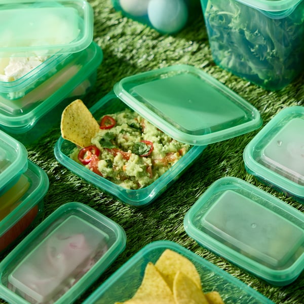 Several green PRUTA food containers with lids on a table. One open container filled with food has its lid resting against it.