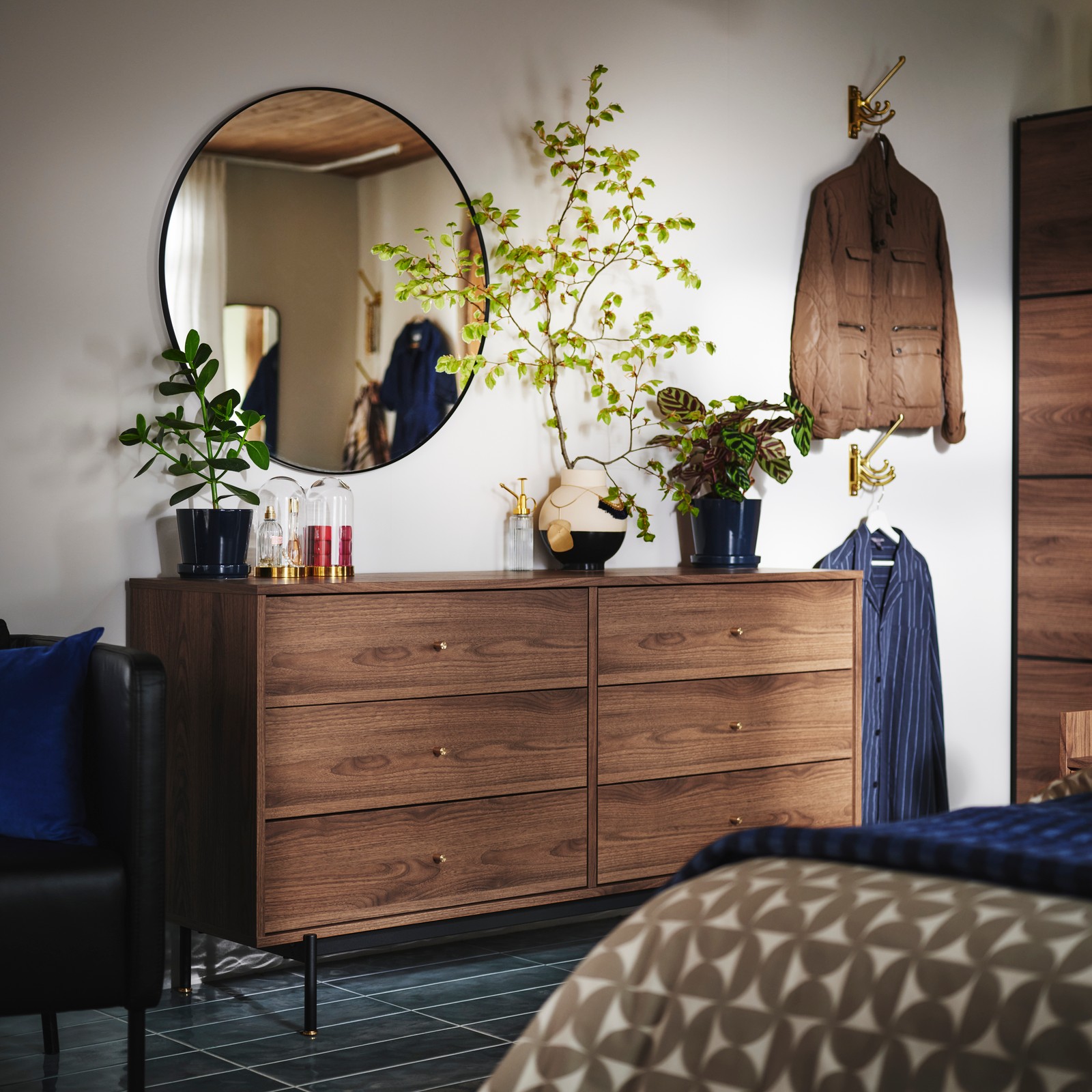 Spavaća soba s plavim podom i belim zidovima. Fokus je na RÅDMANSÖ komodi s fiokama od orahovine, s ogledalom i ukrasima odozgo.