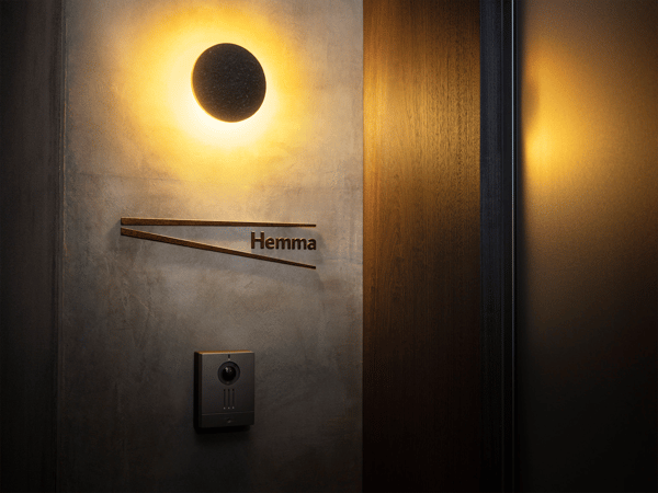 ダークブラウンの壁に取り付けたウォールランプが、あたたかい光で玄関まわりをやわらかく照らすエントランス