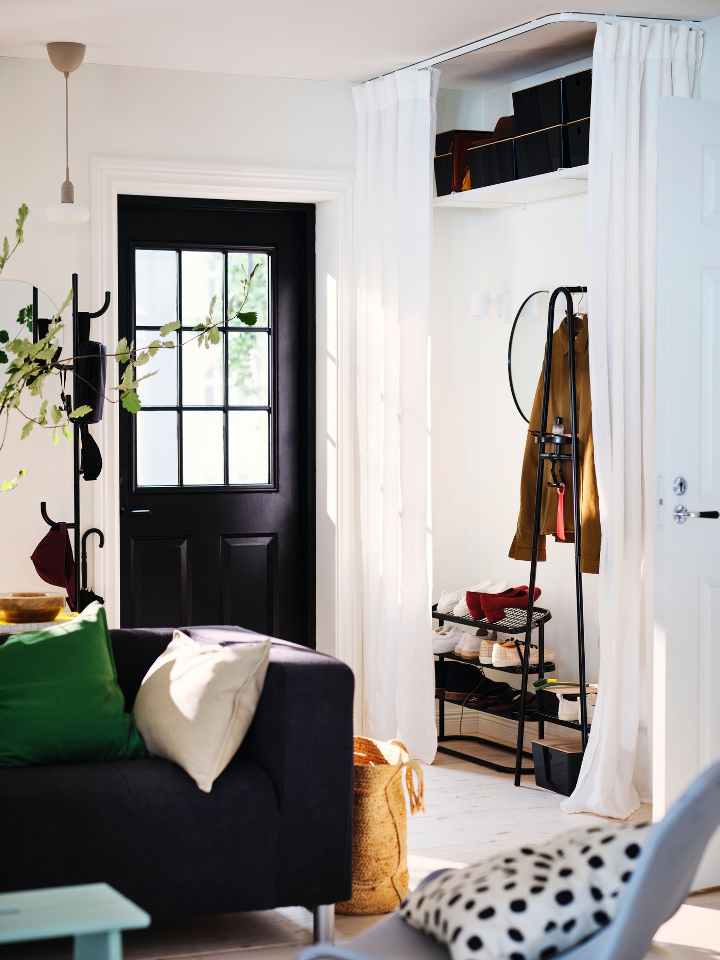 An entryway in a living room with an ÄLGANÄS clothes rack with shoe storage against the wall, framed by a DYTÅG curtain.
