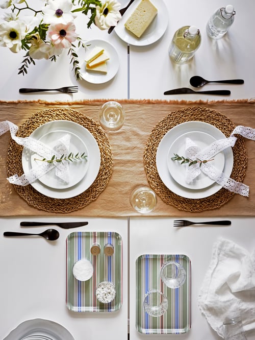 Top shot of a dining setup featuring two white plates, two deep plates, multiple glasses, cutlery, and two trays.