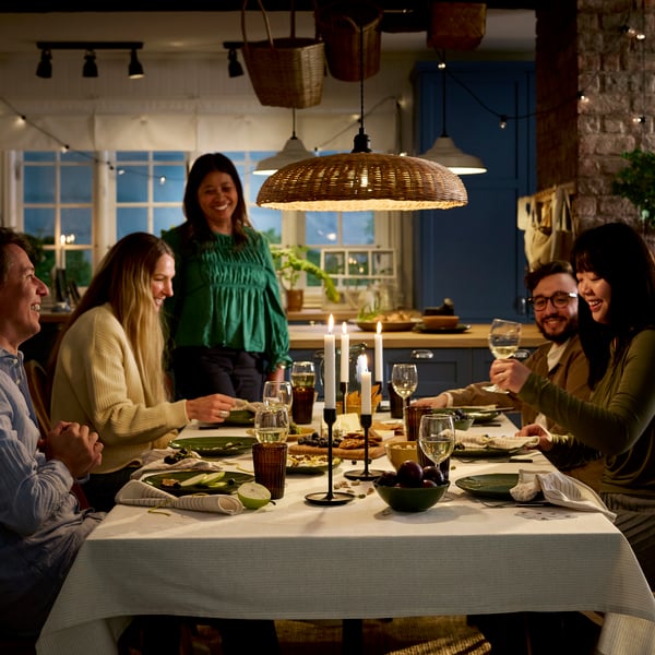 People are gathered around a dinner table for a meal of cheese and fresh fruit, all in a cosy, atmosphere with candles.