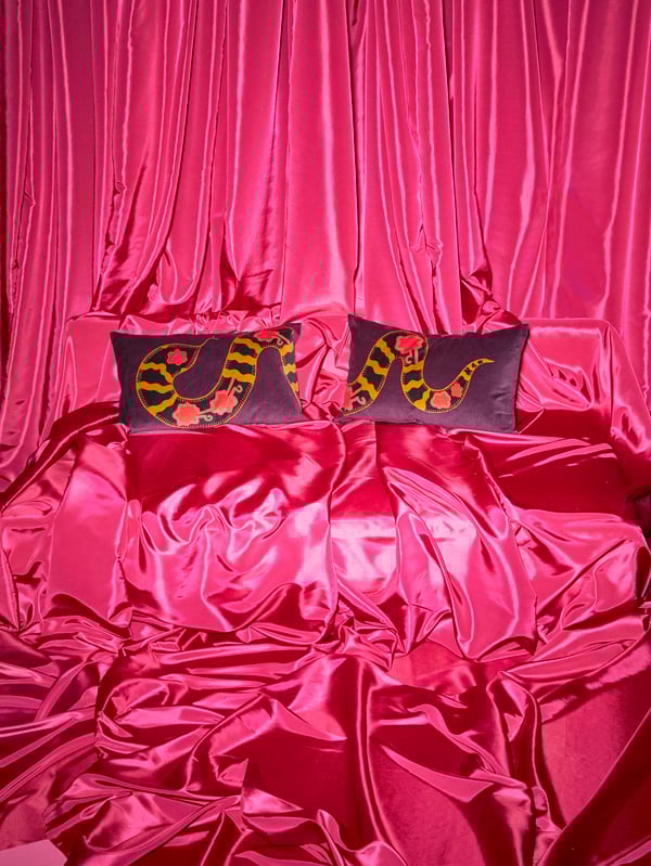Two purple KARISMATISK cushion covers with snake patterns are on a sofa completely covered in pink satin.
