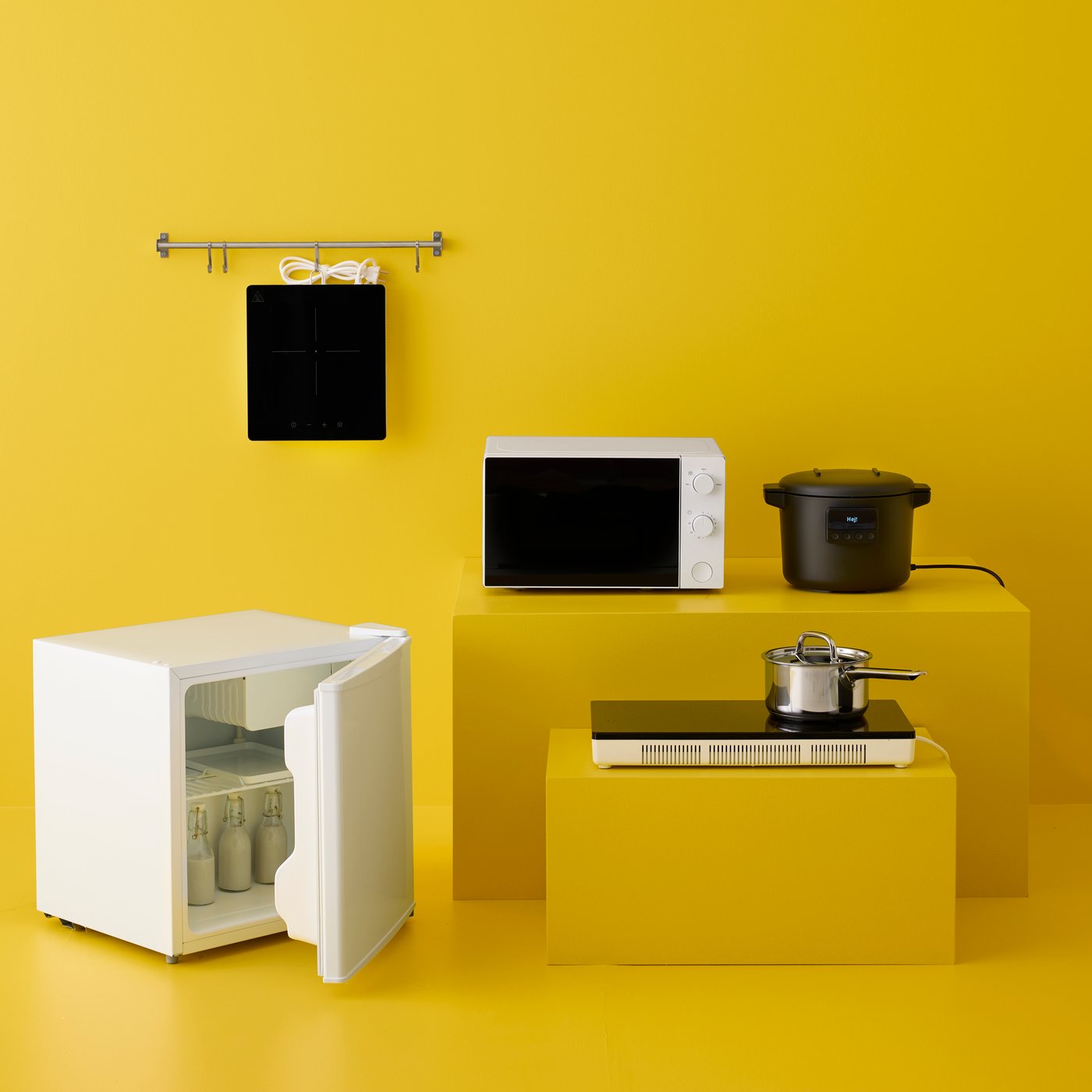 A kitchen set up with yellow walls featuring a white TILLREDA microwave oven next to a rice cooker and an induction hob.