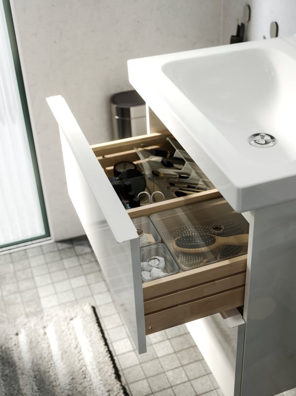 A white GODMORGON sink with an open drawer, revealing beauty products neatly organized in see-through boxes.