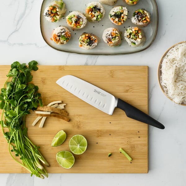 A kitchen countertop features a black VÖRDA vegetable knife alongside fresh herbs and lime, ready for meal preparation.
