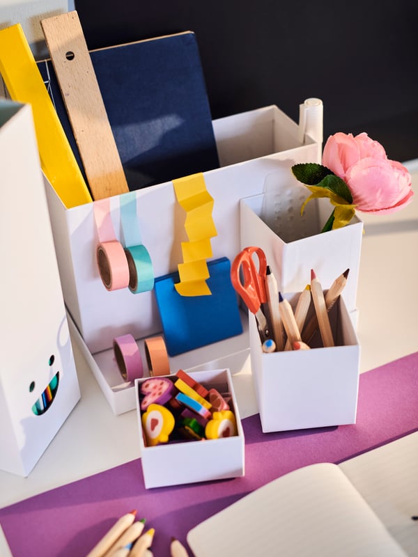 A child's desk space with a white TJENA desk organiser filled with colourful accessories.